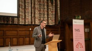 Niels Peek, Professor of Data Science and Healthcare Improvement, giving a lecture in front of a wooden podium at THIS Institute and Homerton College's annual lecture.